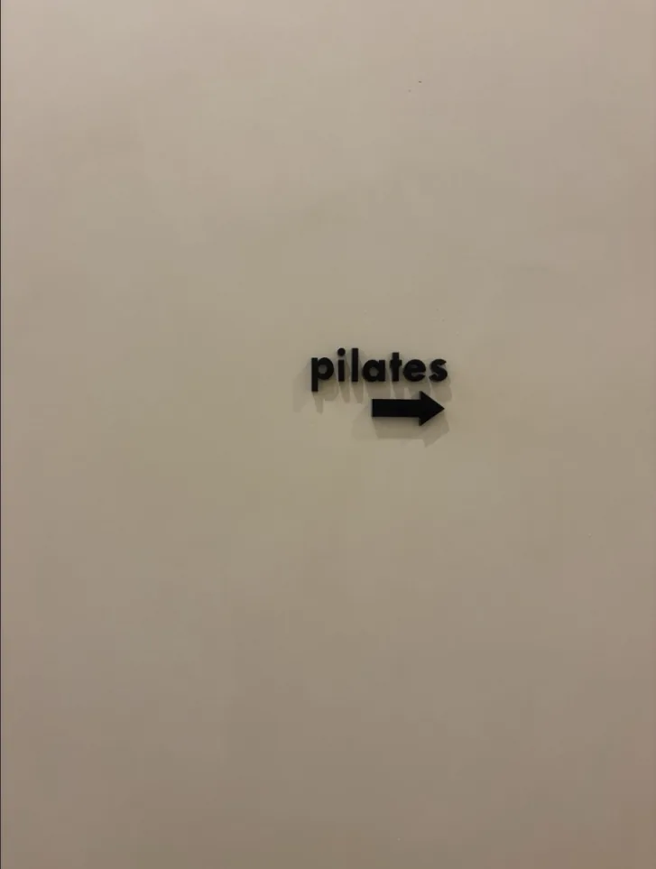 Rótulo de pilates con una flecha en una pared crema